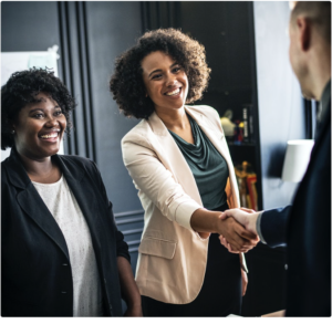 Two professionally dressed women smiling, one is shaking hands with third person
